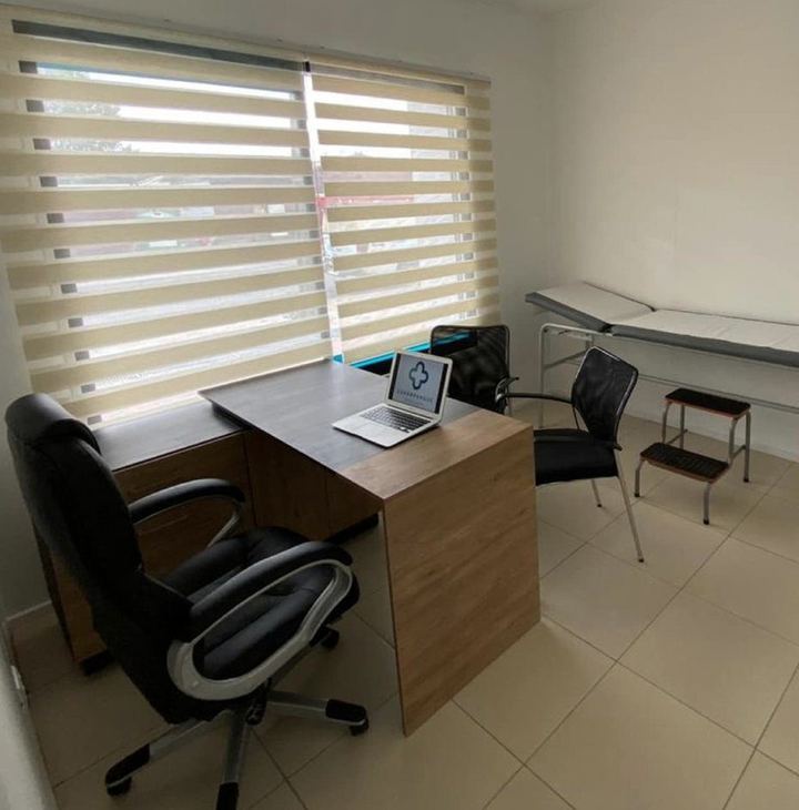 Box de atención del Centro Médico Carampangue: escritorio de madera, camilla y ventana con cortina, con luz natural.