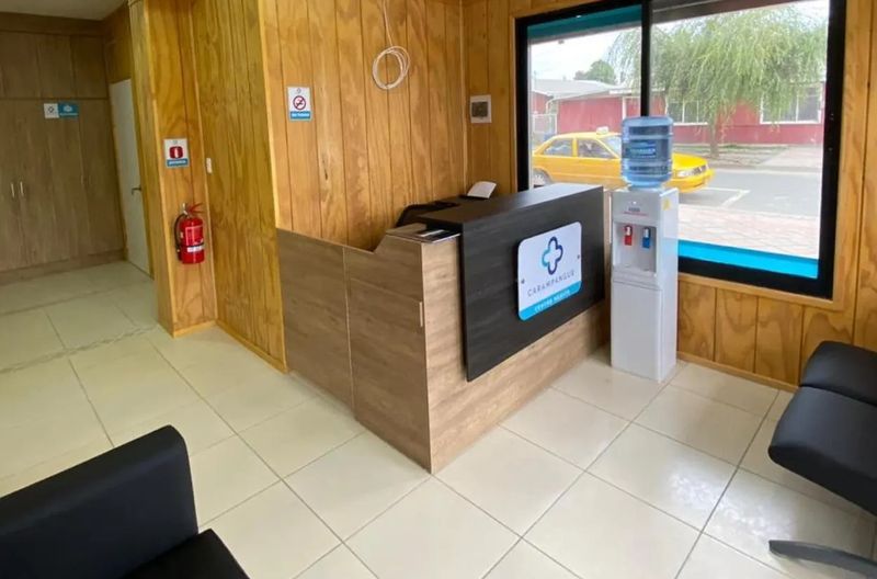 Recepción del centro: mesón de madera, dispensador de agua y ventanal hacia la calle con un taxi colectivo amarillo.