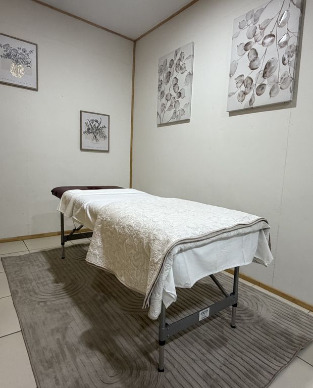 Box de masoterapia del Centro Médico Carampangue: camilla con manta, alfombra y cuadros de flores.