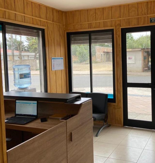 Recepción del centro revestida en madera, con mesón, sillones y ventanales hacia la calle.