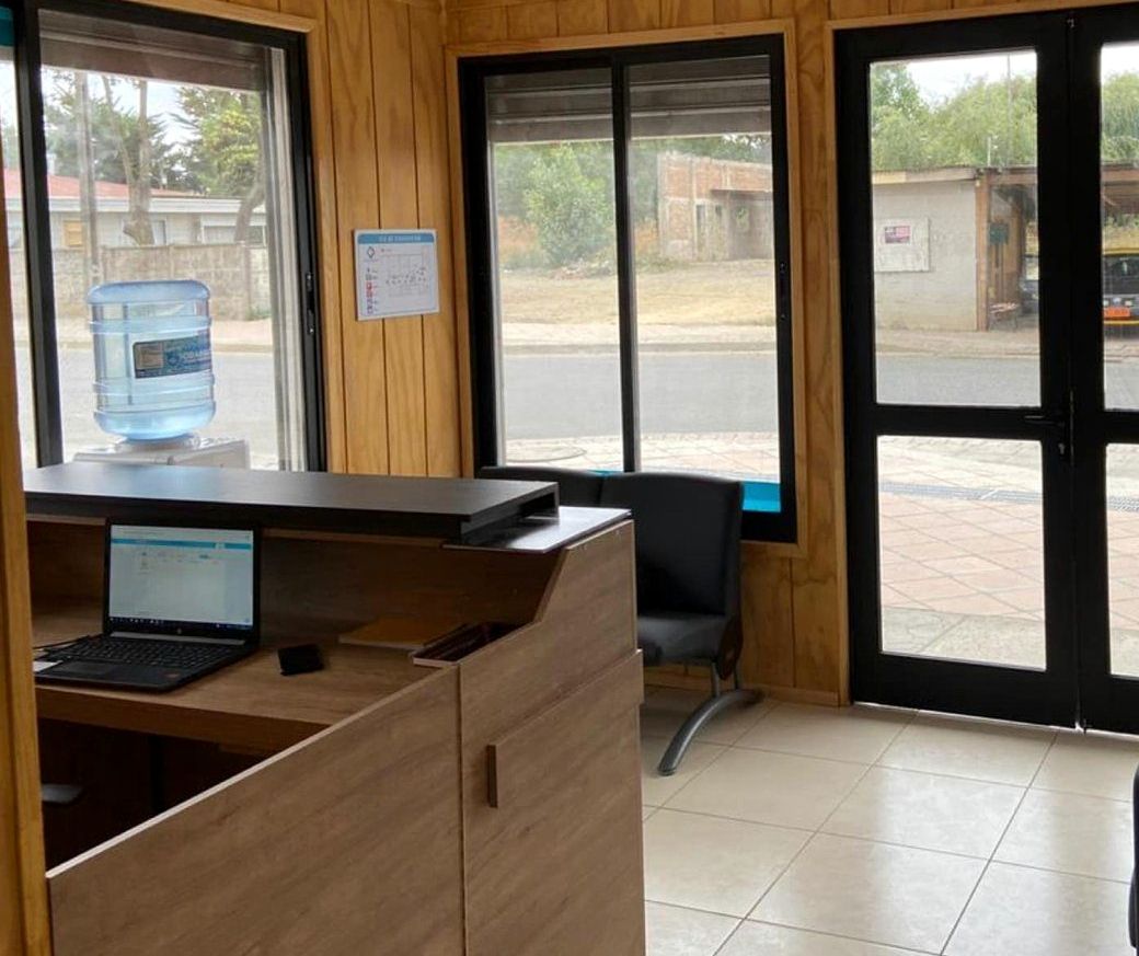 Sala de espera del Centro Médico Carampangue: paredes de madera, mesón de recepción, sillas y ventanales con vista a la calle.