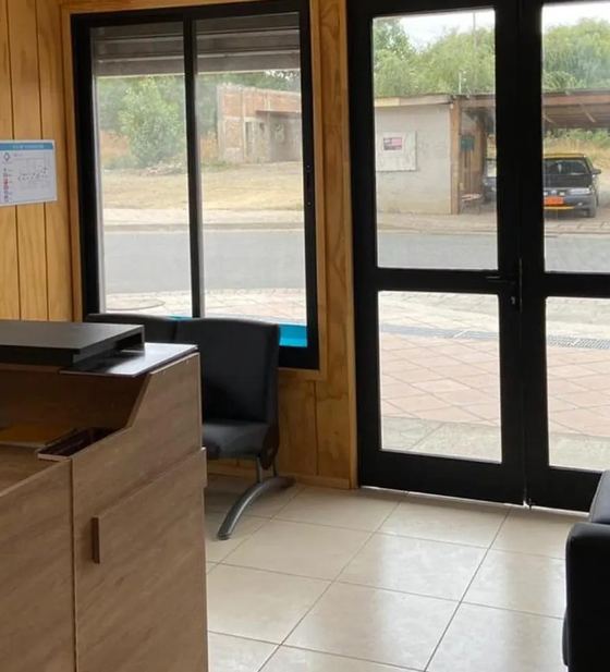 Sala de espera del Centro Médico Carampangue: muros de madera clara, sillas y la puerta de vidrio que da a la calle Monsalve.